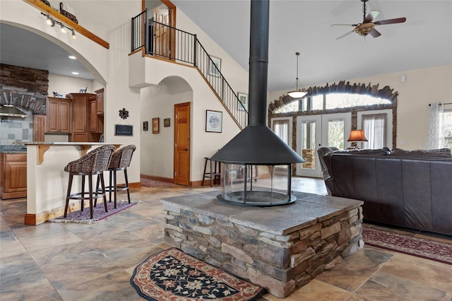 living room with a wood stove, baseboards, a towering ceiling, arched walkways, and ceiling fan