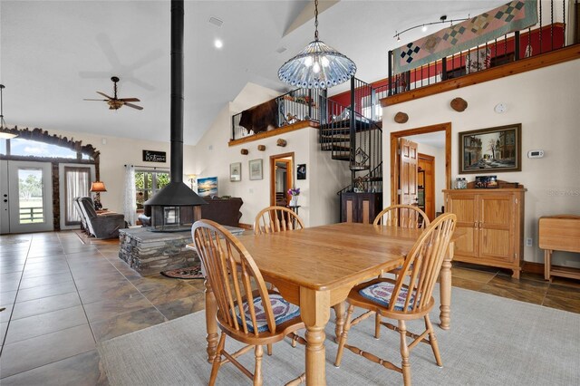 dining space featuring high vaulted ceiling, a wood stove, stairway, and a ceiling fan