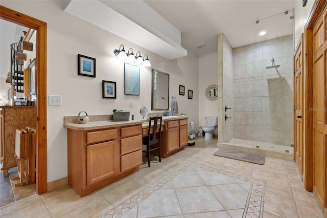 bathroom featuring tile patterned floors, toilet, tiled shower, vanity, and baseboards