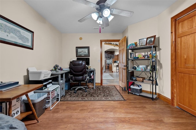 office area featuring a ceiling fan, arched walkways, baseboards, and light wood finished floors