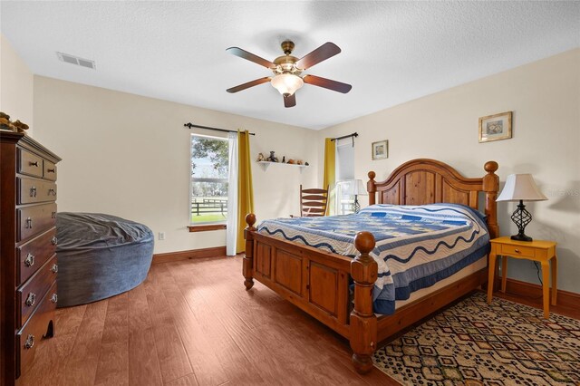 bedroom with baseboards, wood finished floors, ceiling fan, and a textured ceiling