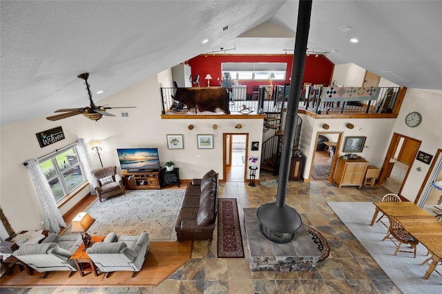 living area featuring high vaulted ceiling, a ceiling fan, a wood stove, stone tile flooring, and visible vents