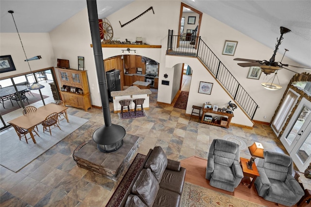 living area featuring ceiling fan, high vaulted ceiling, arched walkways, and a wood stove