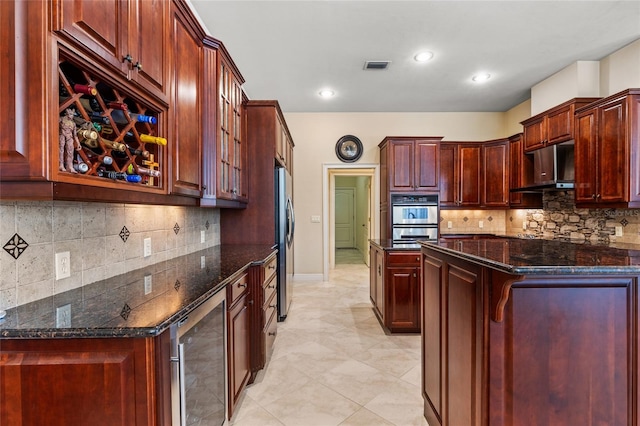 kitchen featuring appliances with stainless steel finishes, beverage cooler, range hood, tasteful backsplash, and visible vents