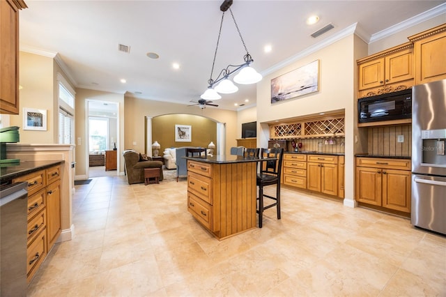 kitchen with ceiling fan, arched walkways, ornamental molding, appliances with stainless steel finishes, and a breakfast bar area