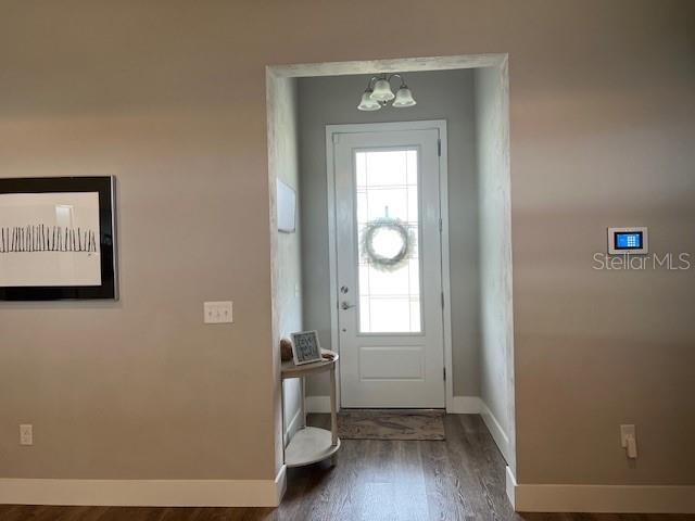 entryway with baseboards, wood finished floors, and a notable chandelier