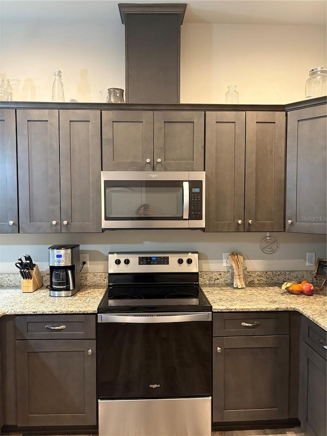 kitchen featuring dark brown cabinetry, appliances with stainless steel finishes, and light stone counters