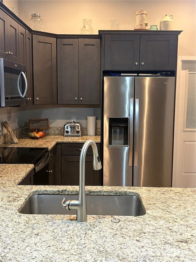 kitchen featuring light stone countertops, a sink, dark brown cabinets, and stainless steel appliances