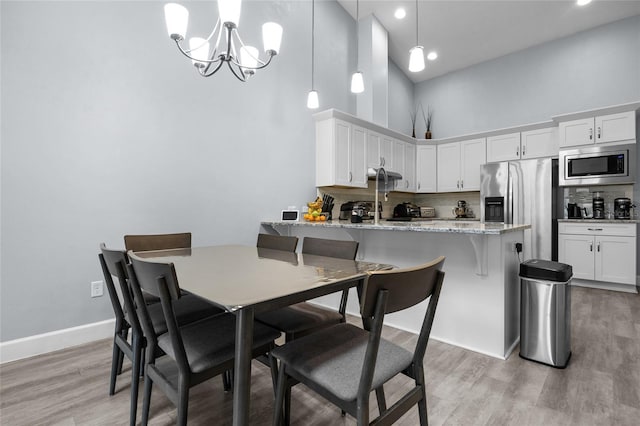 dining space featuring a high ceiling, baseboards, a chandelier, and light wood-type flooring