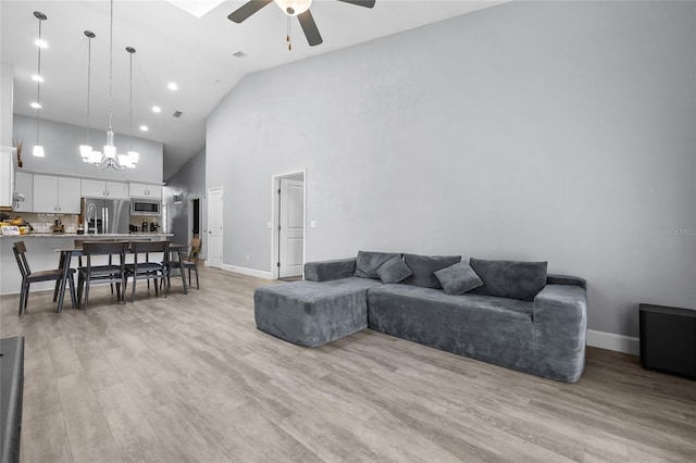 living area with high vaulted ceiling, ceiling fan with notable chandelier, baseboards, and light wood finished floors