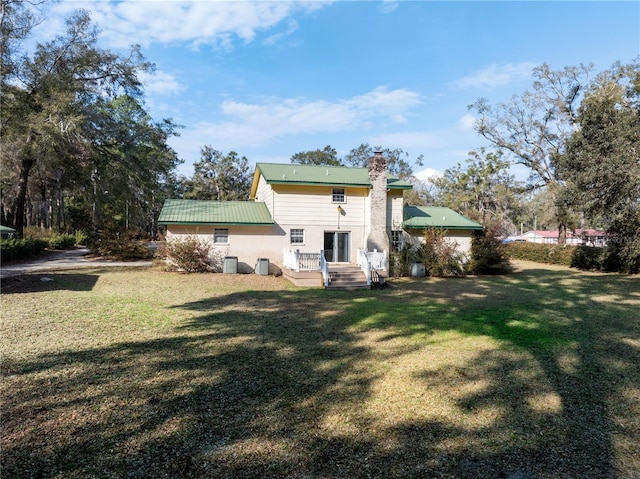 rear view of house featuring metal roof, central AC, a chimney, and a lawn