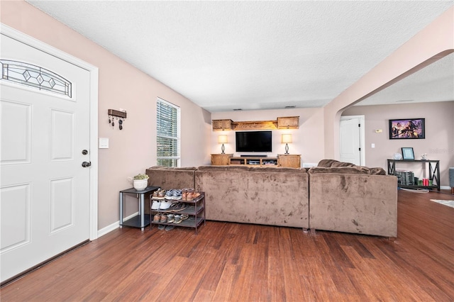 living area with a textured ceiling, wood finished floors, baseboards, and arched walkways