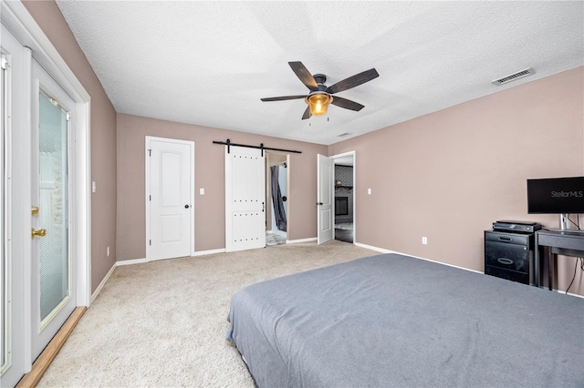 bedroom with baseboards, a textured ceiling, a barn door, visible vents, and light colored carpet