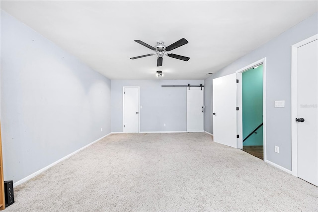 carpeted empty room with baseboards, a ceiling fan, and a barn door