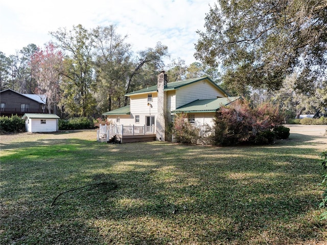 exterior space with a chimney, a front lawn, a shed, a wooden deck, and an outbuilding