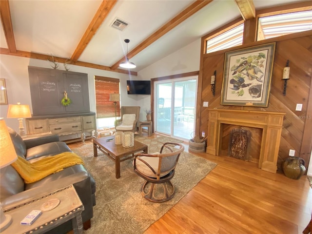 living area featuring lofted ceiling with beams, visible vents, wooden walls, a fireplace, and wood finished floors