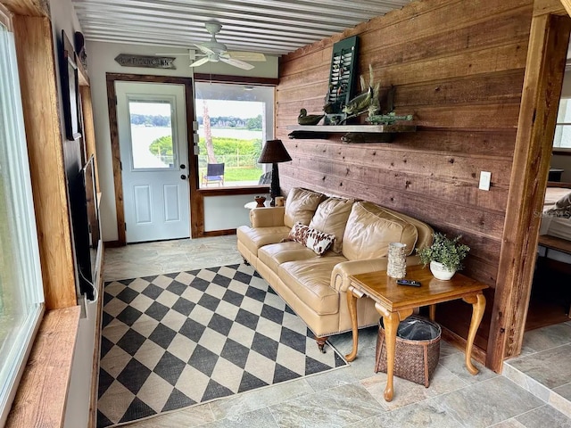 living room with stone finish floor, wood walls, and a ceiling fan