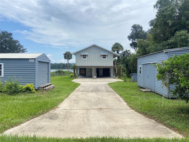 view of front facade featuring an outbuilding, concrete driveway, a storage unit, and a front lawn