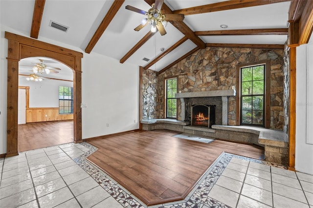 unfurnished living room featuring a wainscoted wall, lofted ceiling with beams, visible vents, ceiling fan, and a healthy amount of sunlight