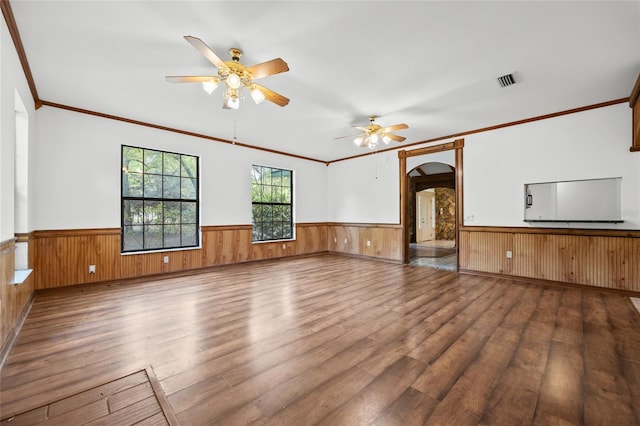 unfurnished living room with a ceiling fan, arched walkways, wood finished floors, and wainscoting
