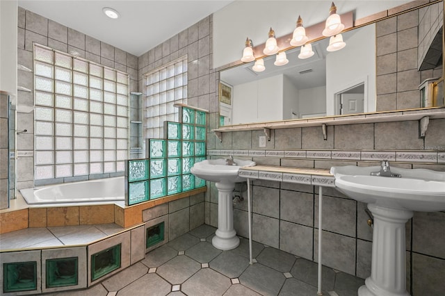 bathroom with a sink, tiled tub, tile patterned flooring, and tile walls