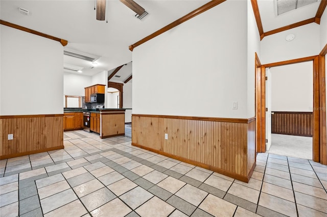 kitchen with a ceiling fan, dark countertops, wood walls, and wainscoting