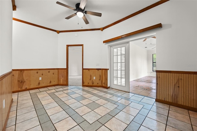 spare room with a wainscoted wall, wood walls, light tile patterned floors, and a ceiling fan