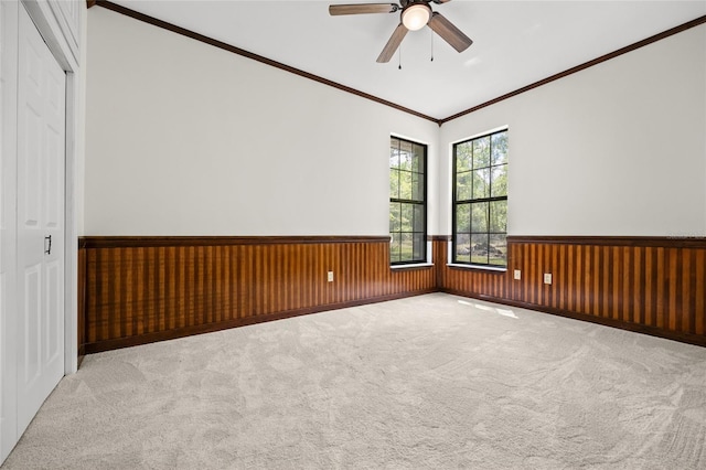 carpeted spare room featuring a ceiling fan, a wainscoted wall, ornamental molding, and wood walls