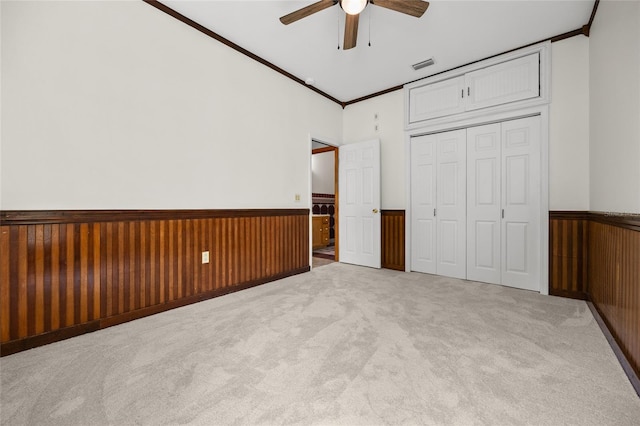 unfurnished bedroom featuring ornamental molding, carpet, a wainscoted wall, visible vents, and a closet