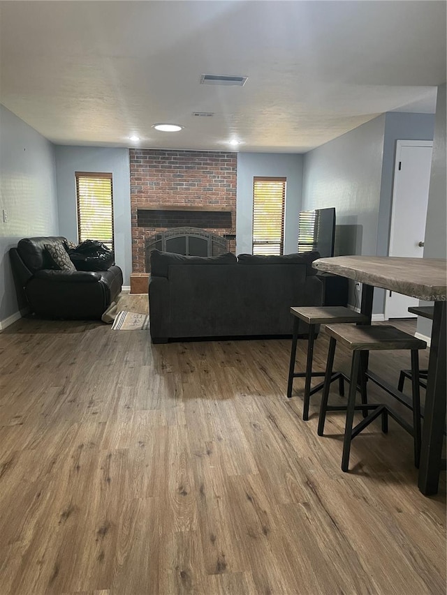 living room with baseboards, a brick fireplace, wood finished floors, and visible vents