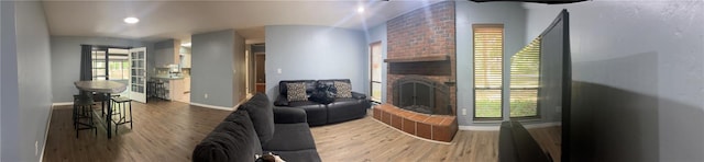 living area with baseboards, a brick fireplace, and wood finished floors