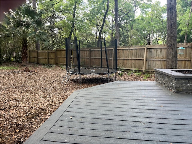 deck with a fenced backyard and a trampoline