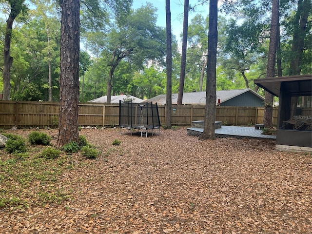 view of yard featuring a deck, a fenced backyard, and a trampoline