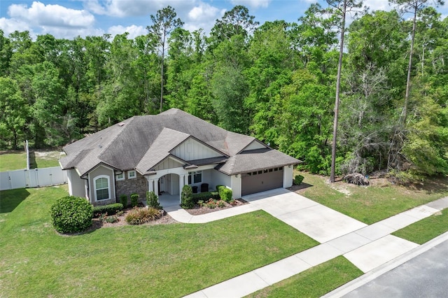 ranch-style house featuring a front lawn, fence, a shingled roof, an attached garage, and driveway