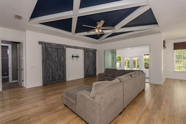 living area featuring visible vents, light wood-style floors, ceiling fan, a barn door, and coffered ceiling