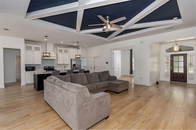 living area with visible vents, baseboards, coffered ceiling, light wood-style flooring, and ceiling fan with notable chandelier