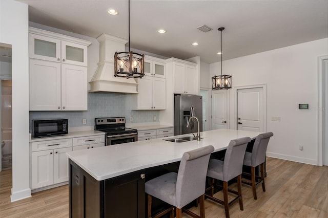 kitchen with a kitchen island with sink, a sink, light countertops, a notable chandelier, and stainless steel appliances