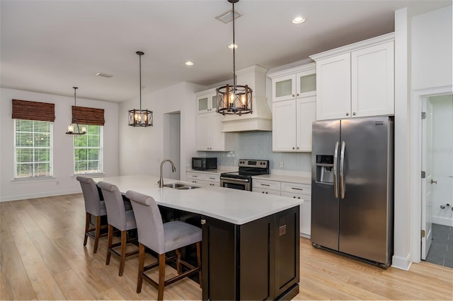 kitchen with appliances with stainless steel finishes, an inviting chandelier, a sink, light wood-style flooring, and backsplash