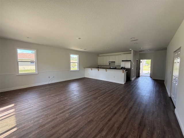 unfurnished living room with dark wood-style flooring, a textured ceiling, recessed lighting, and baseboards