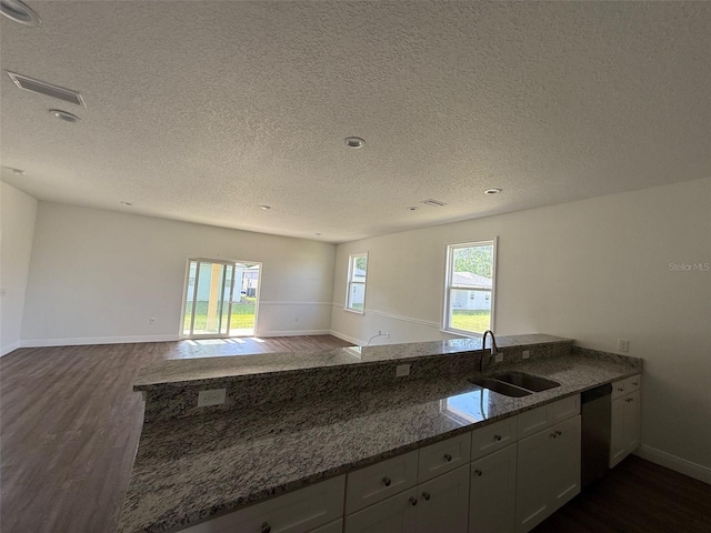 kitchen featuring a sink, dark wood finished floors, dark stone counters, stainless steel dishwasher, and visible vents