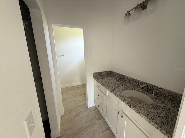 bathroom with vanity, baseboards, and a walk in closet