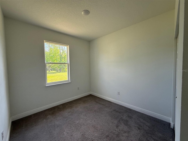 spare room with a textured ceiling, baseboards, and dark carpet
