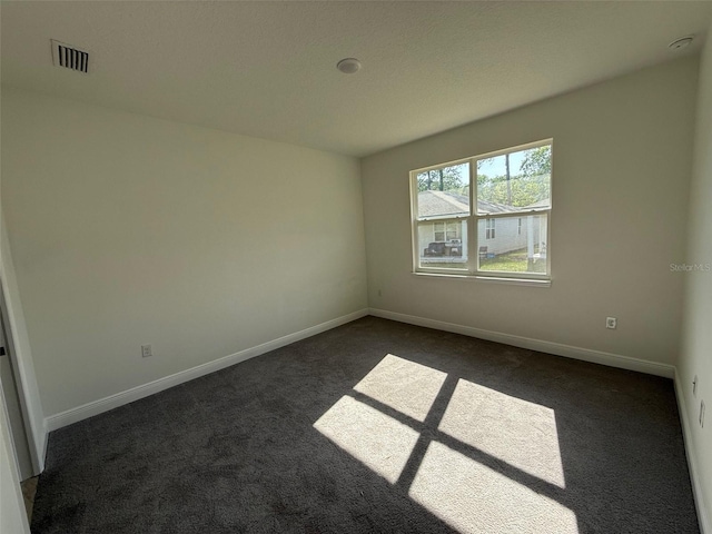 spare room with baseboards, visible vents, and dark colored carpet
