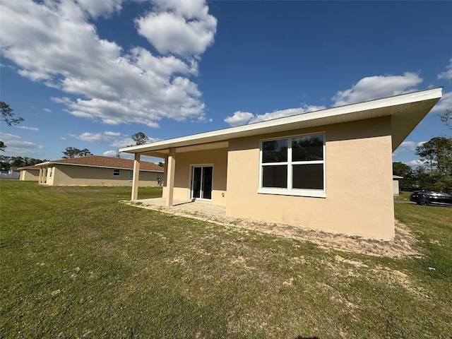 back of house featuring stucco siding and a yard