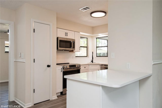 kitchen featuring a peninsula, visible vents, white cabinets, appliances with stainless steel finishes, and wood finished floors