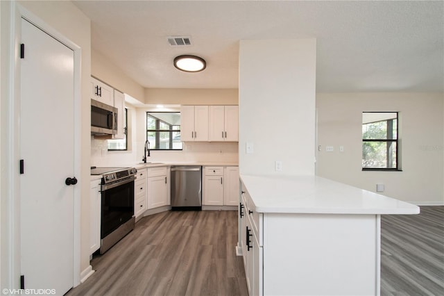 kitchen featuring a peninsula, light wood-type flooring, visible vents, a sink, and stainless steel appliances