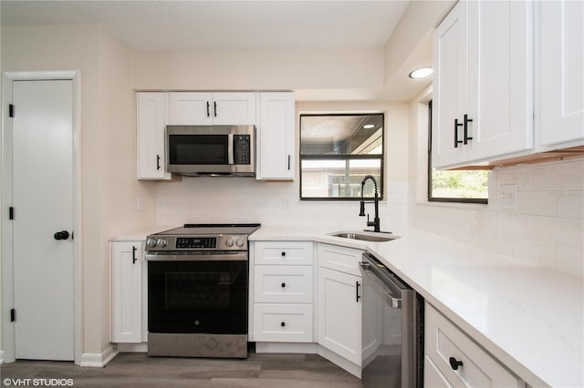 kitchen with appliances with stainless steel finishes, wood finished floors, a sink, and white cabinetry