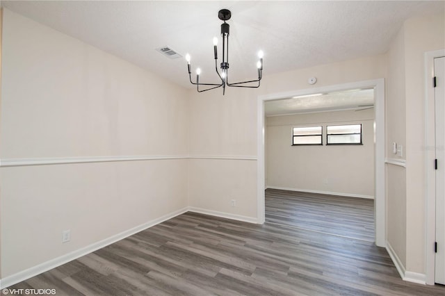 unfurnished dining area featuring visible vents, baseboards, a notable chandelier, and wood finished floors