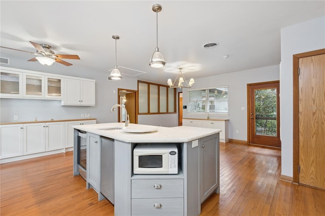 2210 NW 6th Pl, Gainesville, FL 32603 - kitchen featuring a sink, white microwave, light wood finished floors, light countertops, and white cabinetry