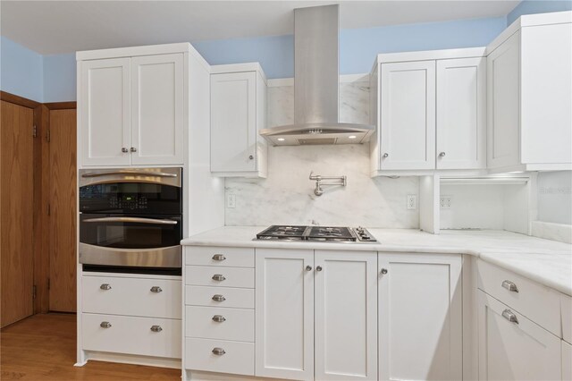 2210 NW 6th Pl, Gainesville, FL 32603 - kitchen featuring stainless steel appliances, ventilation hood, white cabinets, light wood-style floors, and tasteful backsplash